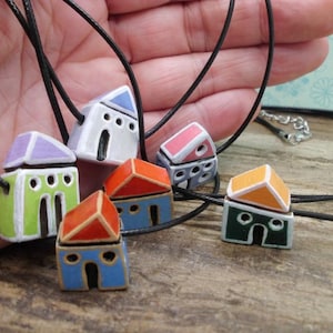 Könnte beinhalten: Ein Set aus sechs bunten Keramik-Hausanhängern an schwarzen Schnüren. Jedes Haus hat eine andere Farbe und ein einzigartiges Design. Die Häuser sind klein und wären ein tolles Geschenk für eine Einweihungsfeier.
