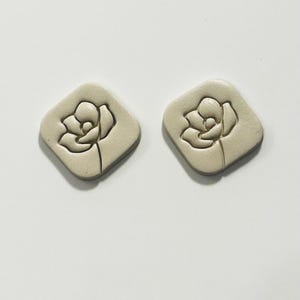 May include: A pair of beige ceramic earrings with a raised floral design.