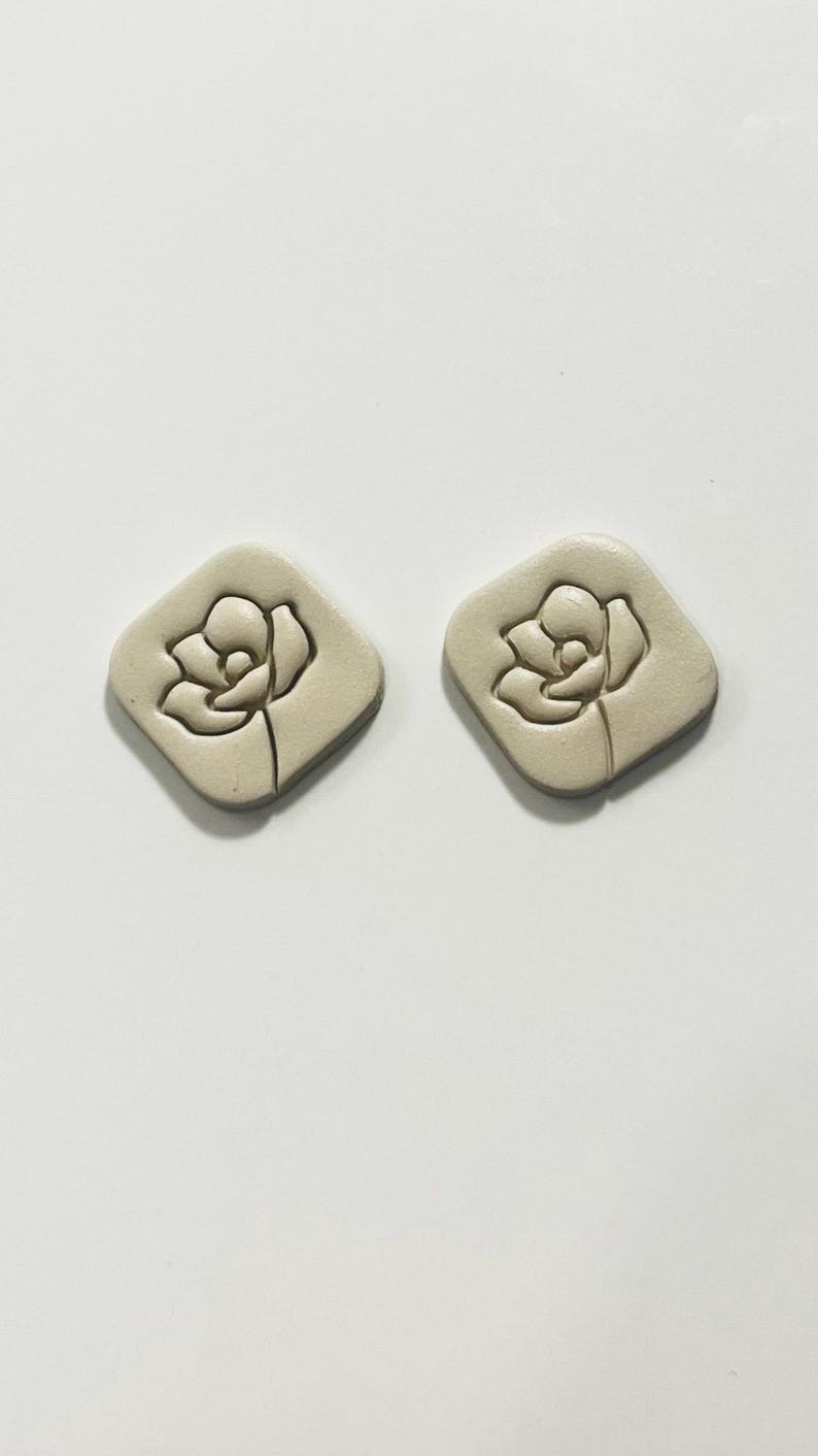 May include: A pair of beige ceramic earrings with a raised floral design.
