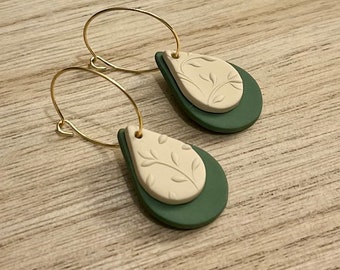 May include: A pair of gold hoop earrings with a teardrop-shaped dangle. The dangle is made of two layers of polymer clay, one green and one white with a leaf pattern.