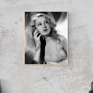 May include: Black and white photograph of a woman with wavy hair, wearing a lace top, looking up and to the left. The photo is framed in a light wood frame.