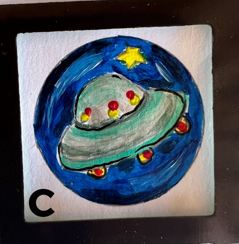 May include: A hand-painted illustration of a flying saucer against a blue and black starry night sky. The saucer is green and gray with red and yellow accents. The image is framed in a black frame with the letter "C" in the lower left corner.
