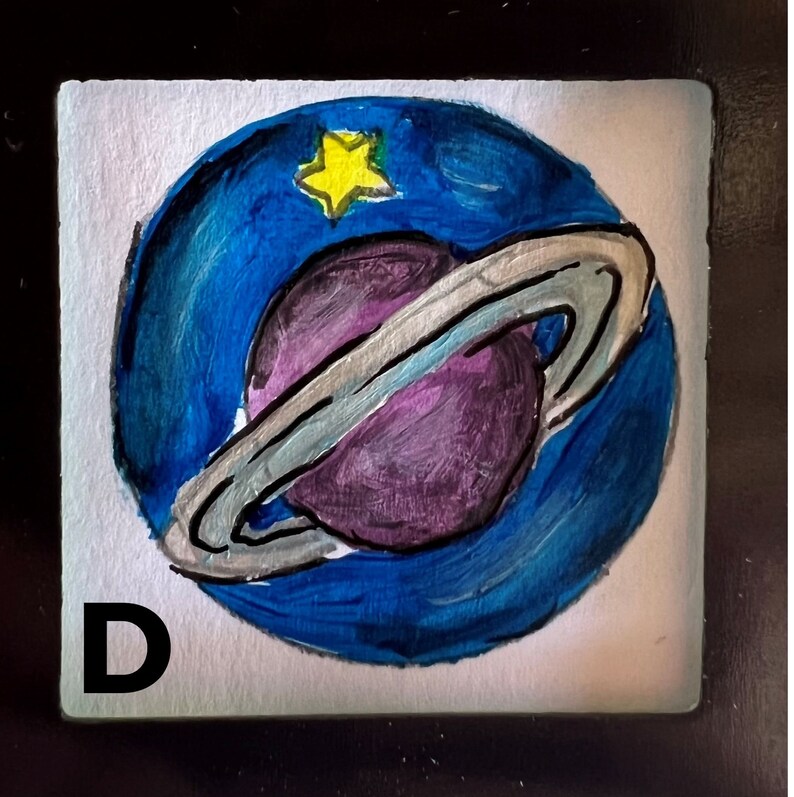 May include: A hand-painted tile with the letter "D" in black and a blue and purple planet with rings and a yellow star in the center.
