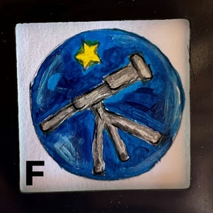 May include: A hand-painted blue circle with a white star and a silver telescope on a white background. The letter "F" is in the lower left corner.