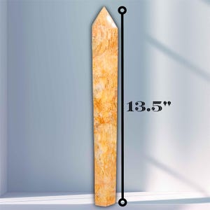May include: A tall, pointed, light-colored stone obelisk, measuring 13.5 inches in height. The obelisk has a textured surface with a mix of light brown and cream colors. The object is set against a light blue background.