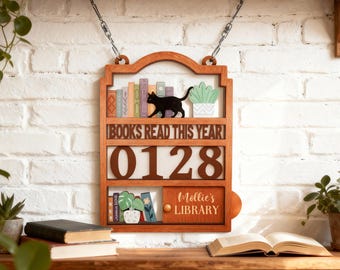 May include: Wooden bookshelf-shaped sign with the text "BOOKS READ THIS YEAR" and the number "0128". The sign features a black cat, miniature books, and a potted plant. The bottom section reads "Mollie's Library".