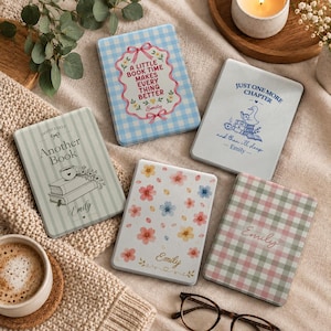 May include: Five rectangular e-reader cases with various designs: a blue gingham case with text A LITTLE BOOK TIME MAKES EVERY THING BETTER, a white case with a duck reading, a striped case with text Another Book, a floral case, and a pink green gingham case.
