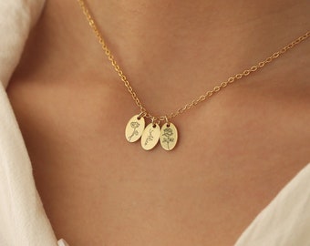 May include: A gold-toned necklace featuring a delicate chain and three small, oval-shaped pendants. Each pendant is engraved with a distinct design: a flower on the left, the name Alice in cursive script in the center, and a rose on the right.