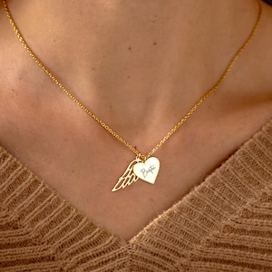 以下が含まれることがあります： ゴールドカラーのネックレス。ハートのペンダントと羽のチャームが付いています。ハートのペンダントには「Bestie」の文字が書かれています。茶色のセーターを着た人がネックレスを着用しています。