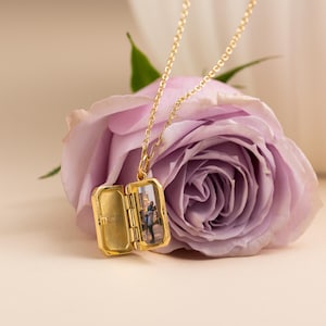 May include: A gold-toned metal locket necklace with a delicate chain. The rectangular locket is open, revealing a small photograph of two people on the right side and the engraved text 'Love you always' on the left interior panel of the locket.