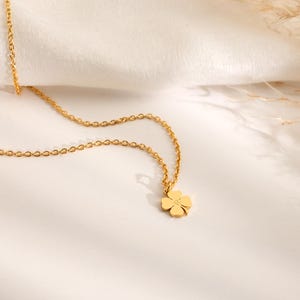 May include: A gold-colored necklace with a four-leaf clover pendant. The chain is delicate and the clover has a small, centered detail. The necklace is displayed on a white surface with soft lighting.