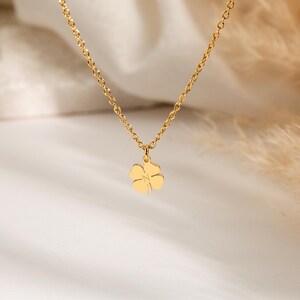 May include: A gold-colored necklace with a four-leaf clover pendant. The chain is delicate, and the clover is a simple, elegant design. The necklace is displayed against a soft, neutral background.
