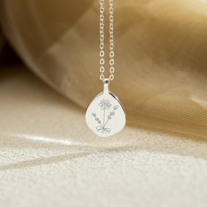 Op de afbeelding: Een zilveren ketting met hanger met een bloemmotief. De druppelvormige hanger is gegraveerd met een bloem en takjes met hartvormige bladeren. De ketting heeft een fijne, zilveren ketting.