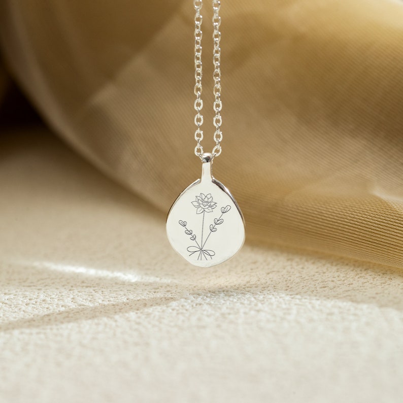 Op de afbeelding: Een zilveren ketting met hanger met een bloemmotief. De druppelvormige hanger is gegraveerd met een bloem en takjes met hartvormige bladeren. De ketting heeft een fijne, zilveren ketting.