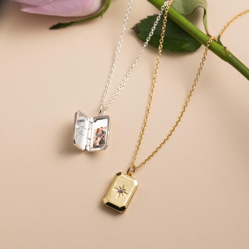 May include: A silver locket necklace with an open rectangular pendant displaying a small photograph inside, and a gold locket necklace with a closed rectangular pendant featuring a central star motif with a tiny purple stone inlay.