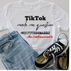 May include: White t-shirt with black text that reads "TikTok made me question: #WHOTFDIDIMARRY Am I still married to". The shirt is paired with blue jeans and black Converse sneakers.