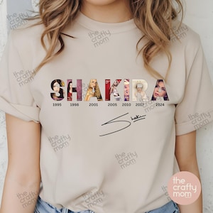 May include: A beige t-shirt with a graphic of the word "SHAKIRA" made up of images from her albums. The years 1995, 1998, 2001, 2005, 2010, 2017, and 2024 are printed below the graphic. The singer's signature is printed below the years.