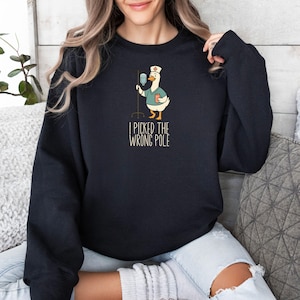 May include: Black sweatshirt featuring a cartoon goose dressed as a nurse, holding an IV drip. The goose is wearing a nurse's cap and scrubs. Text on the sweatshirt reads "I PICKED THE WRONG POLE".