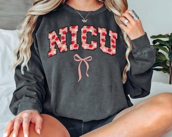 May include: A dark grey sweatshirt with a pink bow and the words "NICU" in white letters with a strawberry pattern.