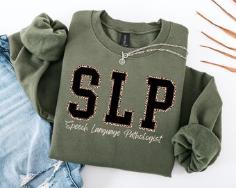 May include: A green sweatshirt with the letters "SLP" in black with a leopard print border. The text "Speech Language Pathologist" is written below the letters.