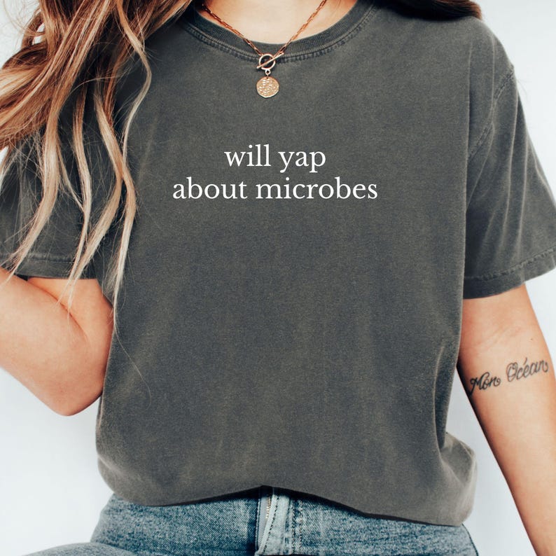 May include: Dark grey t-shirt with the phrase "will yap about microbes" printed in white. The shirt has short sleeves and a crew neck. The shirt is made of a soft, comfortable material.