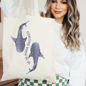 May include: A white tote bag with two blue whale sharks printed on it. The bag has the text "Everything Whale Be Ok" printed on it.