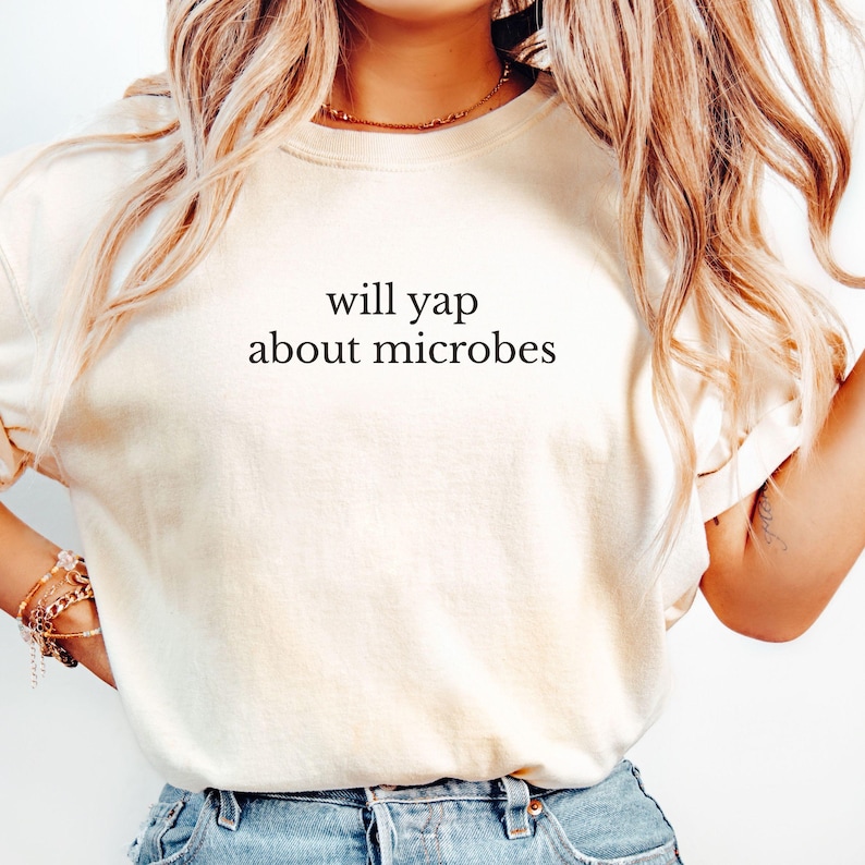 May include: Cream-colored t-shirt with the text "will yap about microbes" in black. The shirt is a casual style, suitable for everyday wear. The text is centered on the front of the shirt.