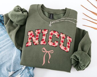 May include: Olive green sweatshirt with a pink and red strawberry print that says "NICU" in a collegiate font. A pink bow is below the text.