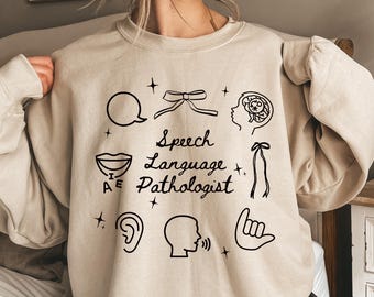 May include: A beige sweatshirt with a black graphic design featuring the text "Speech Language Pathologist" and various symbols related to speech therapy, including a speech bubble, a brain, a bow, a mouth, an ear, a hand, and a person speaking.