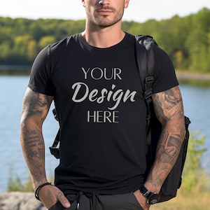 Może przedstawiać: Czarny t-shirt z nadrukiem "YOUR Design HERE" z przodu. Koszulkę nosi osoba z tatuażami na ramionach.