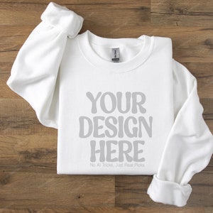 May include: A white crew neck sweatshirt with the text "YOUR DESIGN HERE" in grey, and the tagline "No AI Tricks, Just Real Picks" below. The sweatshirt is on a wooden surface.