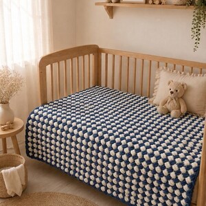 May include: A wooden baby crib with a blue and white checkered blanket. A beige teddy bear sits on a pillow inside the crib. A shelf above the crib holds a framed bunny print, a stuffed bunny, and other decorative items.