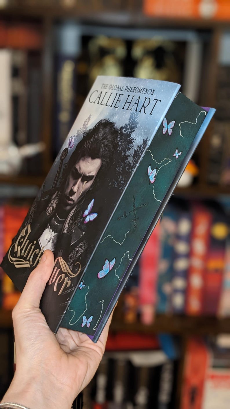 Puede incluir: Un libro titulado "Quick Silver" de Callie Hart. La portada presenta una ilustraci&oacute;n oscura de una persona con una espada, rodeada de mariposas. El lomo es verde oscuro con detalles de mariposas y el texto "Quick Silver".