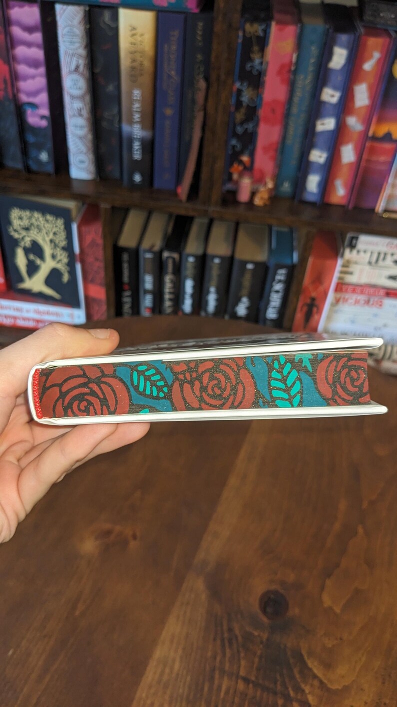 Puede incluir: Primer plano del lomo de un libro con un dise&ntilde;o floral rojo, blanco y turquesa. El dise&ntilde;o presenta rosas y hojas.