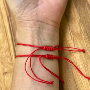 K&ouml;nnte beinhalten: Drei rote Armb&auml;nder aus Schnur, die um ein Handgelenk gebunden sind. Die Armb&auml;nder bestehen aus d&uuml;nner roter Schnur und haben Knoten an den Enden.
