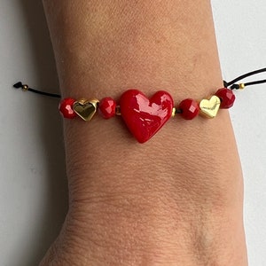 May include: A red heart charm bracelet with gold heart accents and red crystal beads. The bracelet is made with black cord.