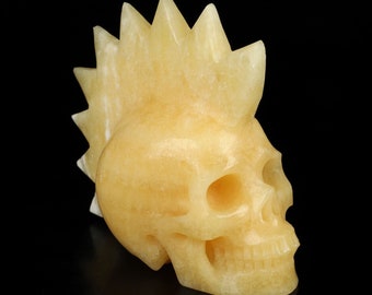 May include: A yellow calcite skull sculpture with a mohawk-style hair design. The skull is carved in detail and has a smooth, polished finish.