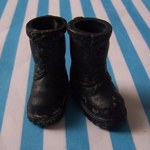 Puede incluir: Un par de botas de cuero negro con acabado texturizado. Las botas tienen una punta redonda y un cierre de cordones.