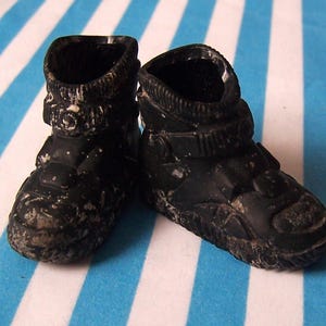 Puede incluir: Un par de botas de cuero negro con una correa de hebilla y una superficie texturizada.