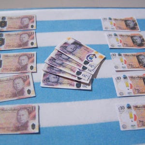 May include: A collection of miniature British banknotes, including denominations of 10 and 50 pounds. The banknotes feature portraits of historical figures and the text "Bank of England".