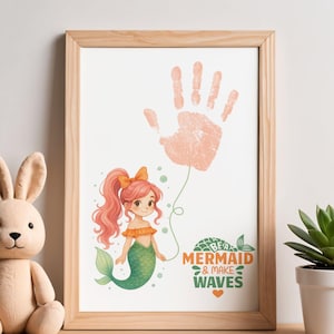 May include: A framed print featuring a handprint resembling a balloon above a cartoon mermaid with pink hair and a green tail. The print includes the text "Be a Mermaid & Make Waves" in orange and green. A plush bunny and a potted succulent are also in the image.