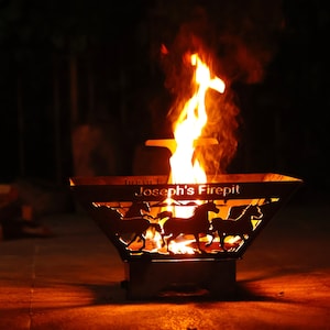 May include: A black metal fire pit with a cutout design of horses and the text "Joseph's Firepit". The fire pit is lit with flames and smoke rising from the center.