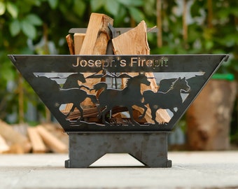 May include: Black metal fire pit with a cutout design of horses and the text "Joseph's Firepit". The fire pit is sitting on a stand and has logs inside.