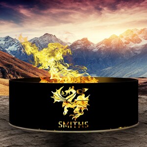 May include: Black metal fire pit featuring a gold dragon design and the inscription "SMITHS" on the front. The fire pit is positioned against a backdrop of snow-capped mountains and a sunset sky.
