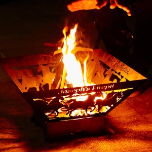 May include: A metal fire pit with a personalised inscription "Joseph's Firepit" and a silhouette of horses. The fire pit is filled with burning flames.