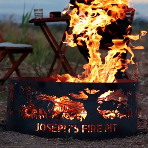 Puede incluir: Un pozo de fuego de metal negro con un dise&ntilde;o recortado de &aacute;rboles y el texto "Joseph's Fire Pit". El pozo de fuego est&aacute; lleno de llamas.