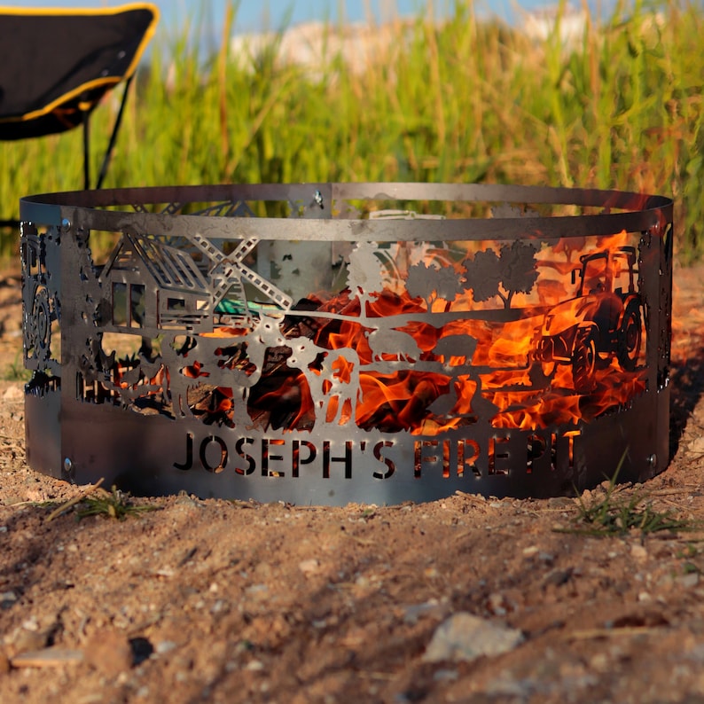 K&ouml;nnte beinhalten: Ein Feuerbecken aus Metall mit einem ausgeschnittenen Design einer Farmszene, einschlie&szlig;lich einer Scheune, einer Windm&uuml;hle und Tieren. Das Feuerbecken brennt mit Flammen und tr&auml;gt den Schriftzug "Joseph's Fire Pit" auf der Vorderseite.