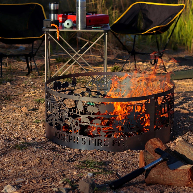 K&ouml;nnte beinhalten: Ein schwarzer Metall-Feuerplatz mit einem ausgeschnittenen Design einer Farmszene. Der Feuerplatz ist mit Flammen gef&uuml;llt und tr&auml;gt die Aufschrift "Joseph's Fire Pit" auf der Vorderseite.