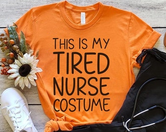 May include: Orange t-shirt with the text "This is my tired nurse costume". A black scrub top, white sneakers, and a stethoscope are also pictured.