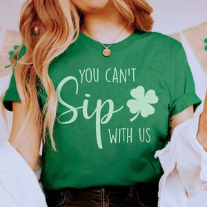 May include: Green t-shirt with the text "You Can't Sip With Us" and a green four-leaf clover graphic.